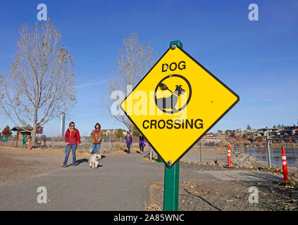 A sign marks a dog crossing area on a walking path along the Deschutes River in Bend, Oregon Stock Photo