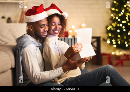 Sweet couple opening Christmas gift, wearing santa hats Stock Photo