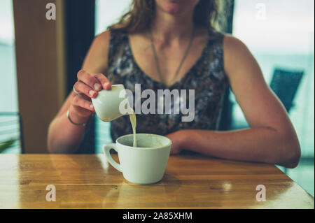 A young woman is pouring cream in her coffee in a cafe Stock Photo
