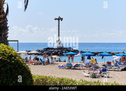 Tenerife, Spain - October 13, 2019: People sunbathing on sandy beach of Playa de los Cristianos, enjoy warm Atlantic Ocean waters, Tenerife, Canary Stock Photo