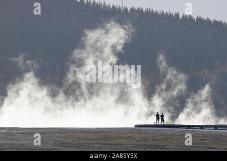 Visitors are silhouetted against plumes of steam at Grand Prismatic Hot Springs in Yellowstone National Park, Wyoming, USA Stock Photo