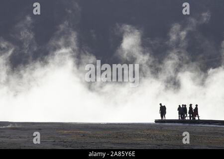 Visitors are silhouetted against plumes of steam at Grand Prismatic Hot Springs in Yellowstone National Park, Wyoming, USA Stock Photo