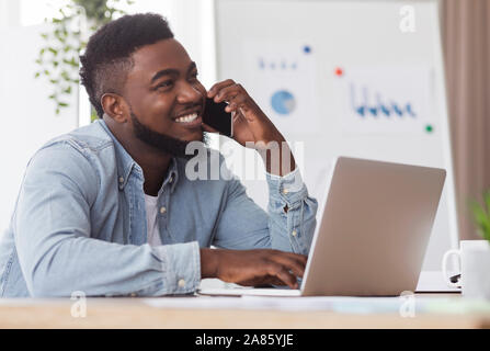African worker talking on cellphone and using laptop in office Stock Photo