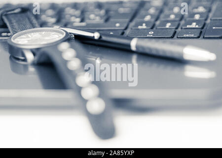 Close-up shot on a laptop, wristwatch and pen, monochrome and mostly blurry image. Stock Photo