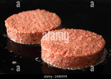 Two uncooked plant based vegetarian burger patties being cooked on flat black iron grill. Stock Photo