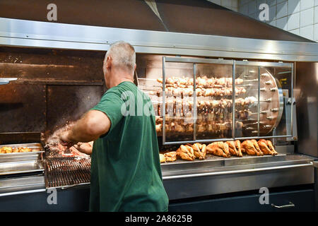 Man from back cooking roast chickens and grilled meat in a rotisserie at San Lorenzo Central Market in the city center of Florence, Tuscany, Italy Stock Photo