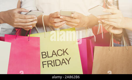Three girls with colorful shopping bags using cellphones Stock Photo