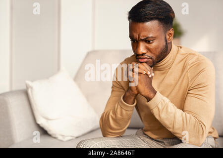 Unhappy Black Man Thinking Sitting On Couch At Home Stock Photo