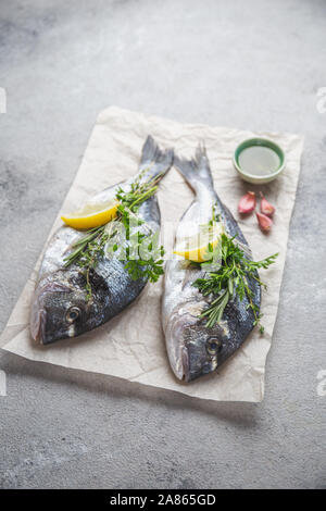 Dorada fish, raw fresh sea bream with lemon and herbs on a grey stone background, top view. Stock Photo