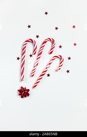 Christmas composition three caramel candy canes, cofetti stars and red bow on white background. Festive minimal style flat lay. For greeting card, inv Stock Photo