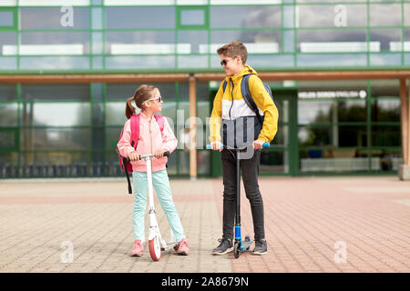 happy school children with backpacks and scooters Stock Photo