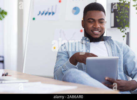 Relaxed african american employee using digital tab at workplace Stock Photo
