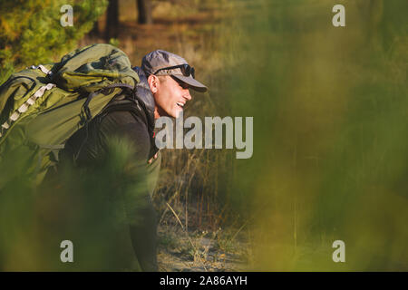 Older man walking in forest with green backpack feeling exhausted Stock Photo
