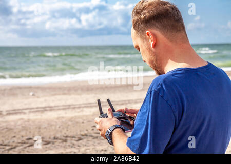 Man flying his drone by using a remote controller on the beach. Stock Photo