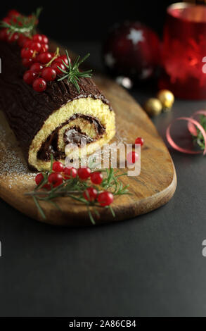 Chocolate Christmas Yule Log, Buche de Noel on wooden cutting board. Christmas decoration on dark background. Closeup Stock Photo