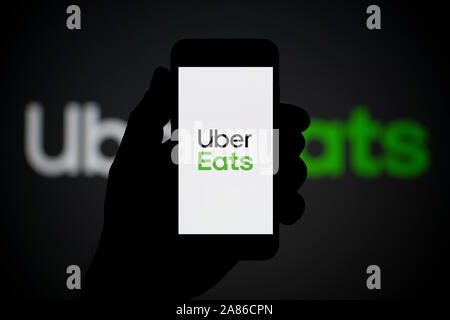 A man looks at his iPhone which displays the Uner Eats logo, with the same logo in the background (Editorial use only). Stock Photo