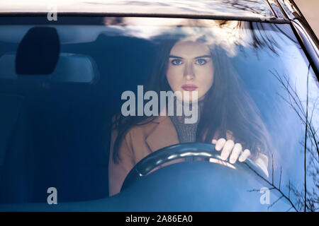 a young woman sitting in a car behind the wheel.she's going to go. in the glass of the car reflection of the sky. Stock Photo