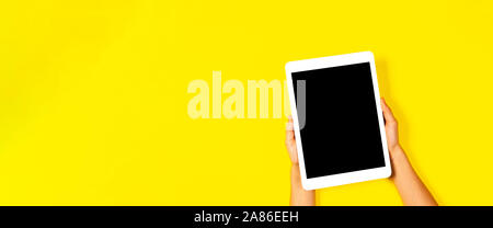 Kid hands holding white tablet computer on yellow background Stock Photo