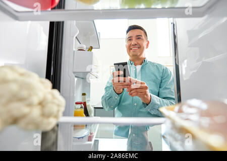 man with smartphone making list of food in fridge Stock Photo