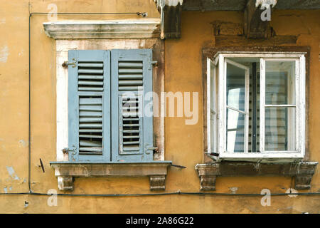 Two old Windows on a wall with peeling yellow plaster in the old part of Rovinj in Croatia. Stock Photo
