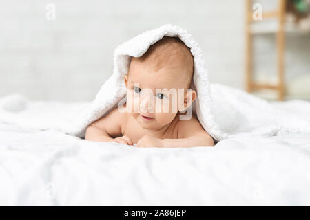 Adorable newborn boy lying on bed under soft white blanket Stock Photo
