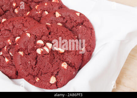 Fresh baked Christmas and Thanksgiving holiday red velvet and macadamia nut cookies served on a white dish towel with a cutting board background. Stock Photo