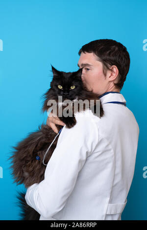 Brunet vet with black cat in his arms on empty blue background Stock Photo