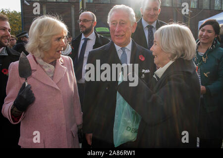 Prince Charles and Camilla the Duchess of Cornwall at the Swiss Cottage farmers market, meeting stall holders. Charles relaxed and laughing, Camilla with a cake cutter. Body guards are standing behind them. Its is the 20th anniversary of London Farmers Market. UK 2019. 2010s HOMER SYKES