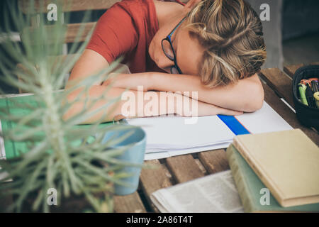 Tired student doing homework at home sitting outdoor with school books and newspaper. Boy weary due to heavy study. Kid asleep on the copybook after l Stock Photo