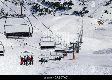PYRENEES, ANDORRA - FEBRUARY 15, 2019: Tourists athletes, skiers and snowboarders on the chair lift of a ski resort. The lift line stretches through t Stock Photo