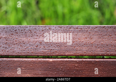Wood planks covered by water drops on green grass background, rainy weather. Brown wooden boards Stock Photo