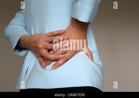 Pain in side, woman in office suit suffering from backache. Female hands holding lower back, concept of kidney or spine disease Stock Photo