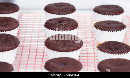 Step by step. Cooling freshly baked chocolate cupcakes on a cooling rack. Stock Photo