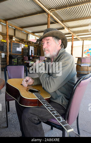 Older man with a guitar sitting outside the iconic Club in the Scrub, the Grawin, Queensland, QLD, Australia Stock Photo