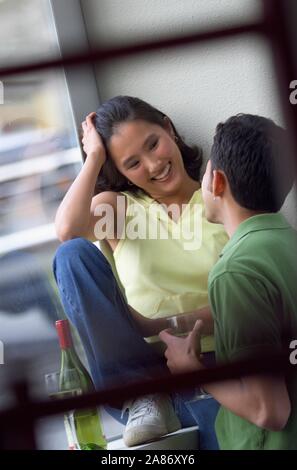 Young attractive Asian couple enjoying the moment with a glass of wine in front of a large window Stock Photo