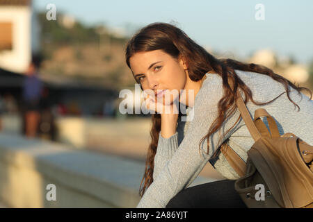 Serious casual girl looks at you at sunset sitting in the street Stock Photo