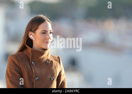 Relaxed woman listening to music using wireless earphones looking away in winter Stock Photo