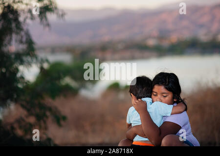 Brother and sister separated from parents are hugging each other in a foreign country, across a river.