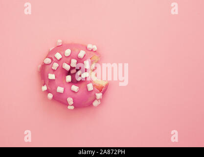 Pink frosted eaten donut with white marshmallows on pink background. Top view, flat lay, copy space. Stock Photo