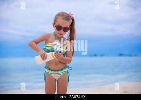 Little cute girl in swimsuit holds suntan lotion bottle Stock Photo