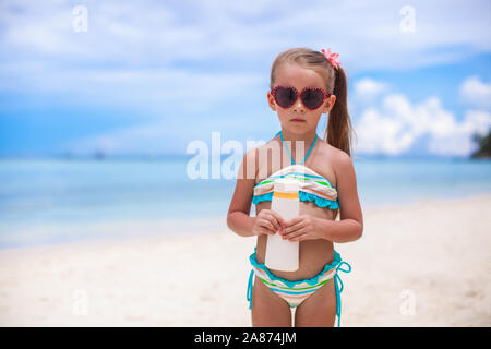 Little cute girl in swimsuit holds suntan lotion bottle Stock Photo