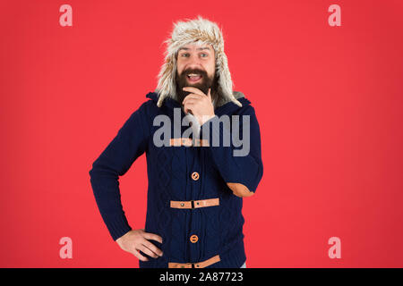 Winter season menswear. Hipster rustic style outfit. Fashion menswear shop. Masculine clothes concept. Winter menswear. Clothes design. Man mature bearded stand warm jumper and hat on red background. Stock Photo