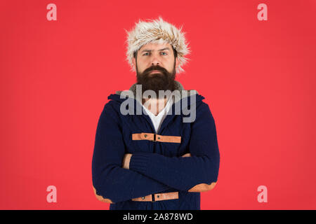 Clothes design. Man bearded stand warm jumper and hat on red background. Winter season menswear. Hipster rustic style furry hat. Fashion menswear shop. Masculine clothes concept. Winter menswear. Stock Photo