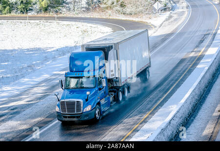 Big rig blue bonnet day cab semi truck with roof spoiler and refrigerator unit on the front wall of reefer semi trailer transporting commercial cargo Stock Photo