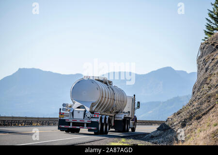 Big rig day cab white semi truck with reinforced tank semi trailer for transportation of dangerous liquid chemical and explosive substances driving on Stock Photo