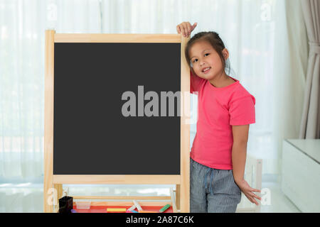 Asian Kindergarten girl child holding blackboard in school room looking happy with big smile. Back to school and education concept. Stock Photo