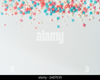Festive border frame of colorful pastel sprinkles on white background, copy space bottom. Sugar sprinkle dots and stars, decoration for cake and bakery. Top view or flat lay