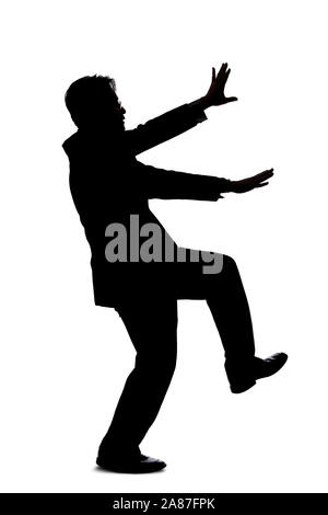 Silhouette of a backlit model posing as a businessman on a white background.  He is balancing or slipping and falling due to an accident Stock Photo