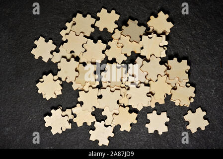 Chaos and confusion: detail of wooden jigsaw puzzle pieces mixed on black background. Concept for disorganization and problems. Stock Photo