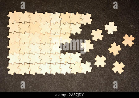 Half ordered puzzle with white jigsaw pieces. One side of the image shows part of the completed puzzle, other side shows the work in progress on a tex Stock Photo